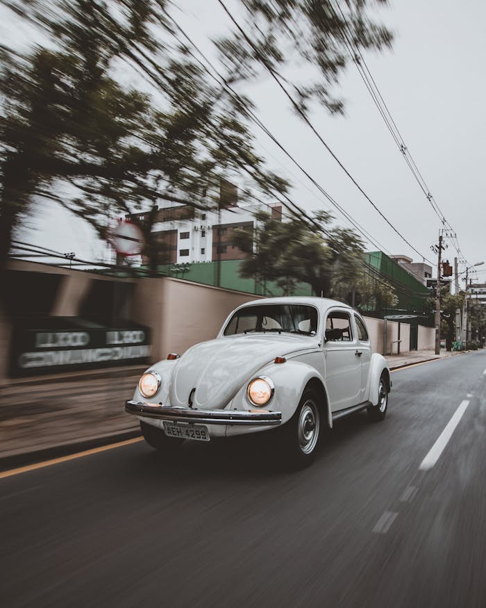 A classic white vintage car driving through the streets of Curitiba, Brazil on a cloudy day.