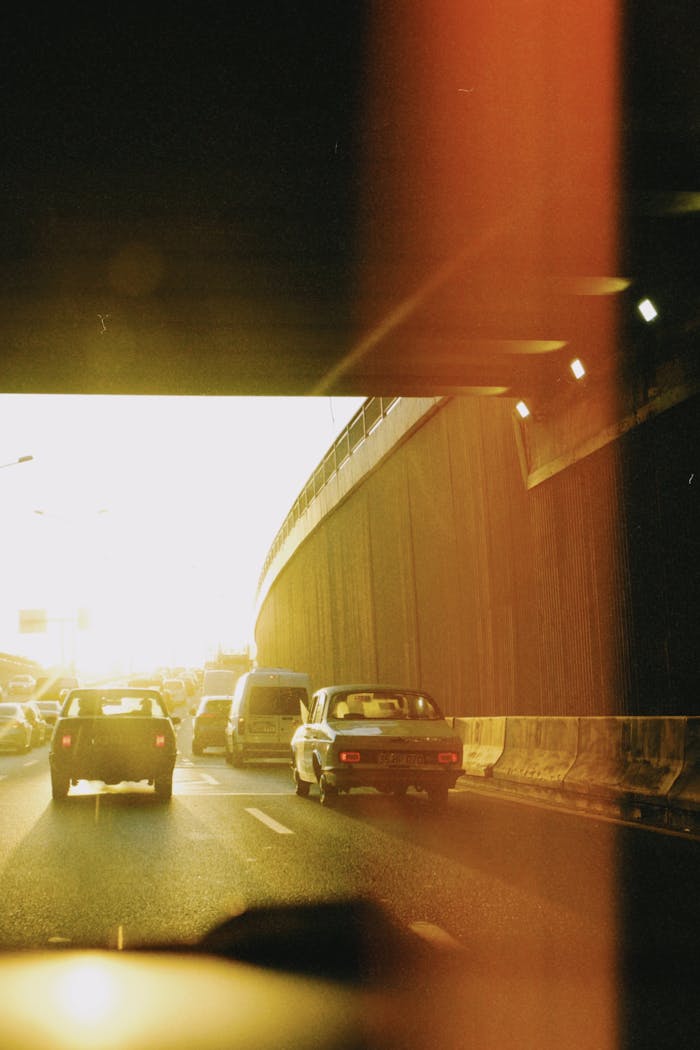 Cars driving through a city tunnel during sunset, casting a warm glow on the road.